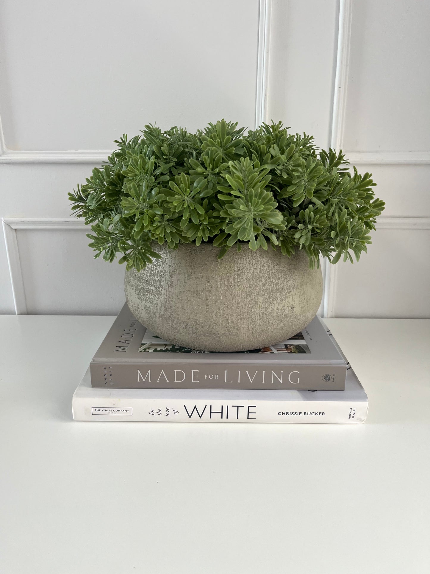 Artificial crossostephium light green succulents set in a beige terracotta bowl planter displayed on a stack of books.