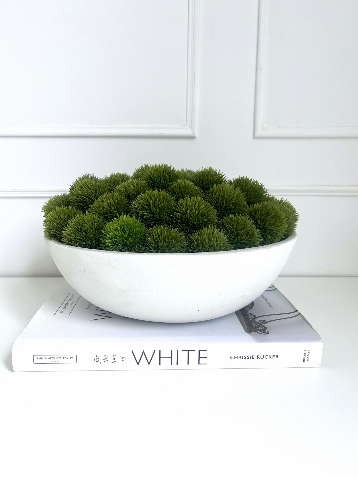 Artificial lush green dianthus set in a large concrete bowl planter displayed on a book.