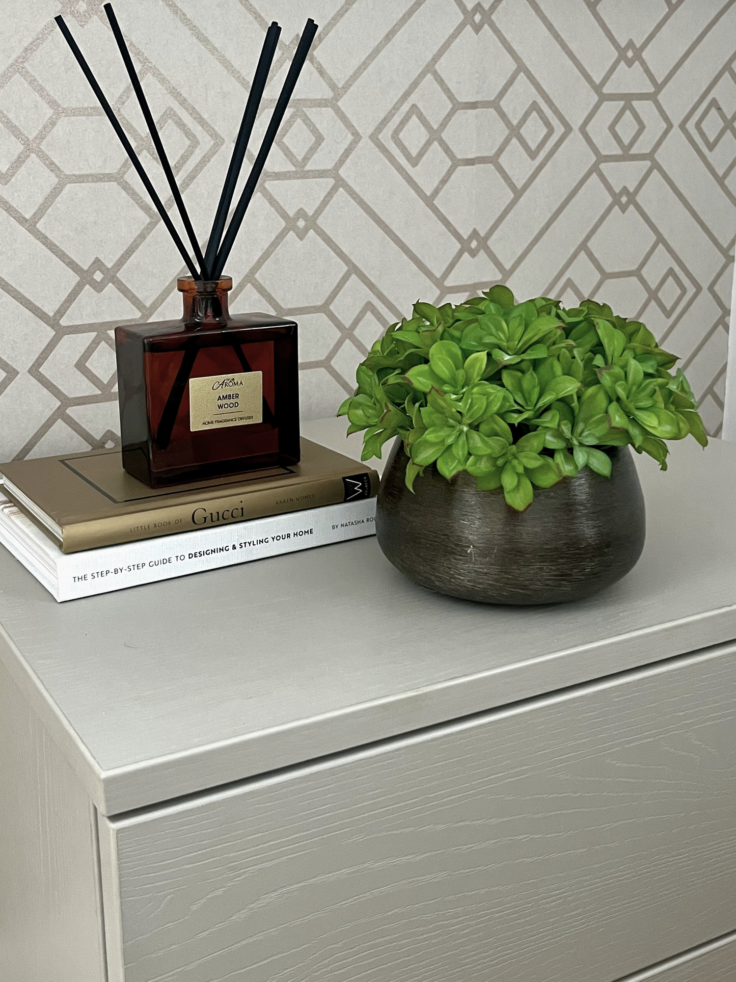 Lush green soft pillow moss displayed in a black mango wood bowl planter displayed next to a reed diffuser on a stack of books.