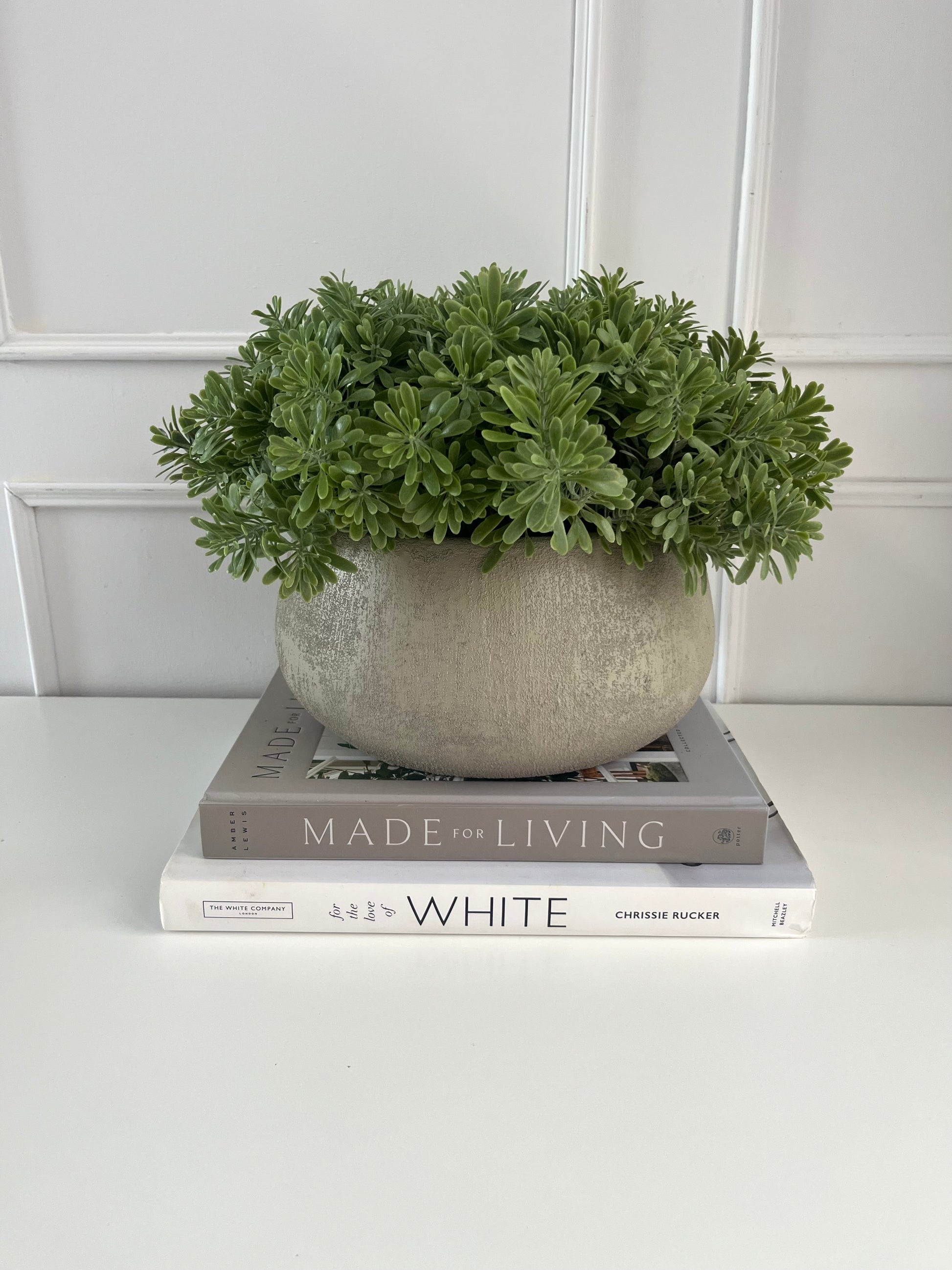 Artificial crossostephium light green succulents set in a beige terracotta bowl planter displayed on a stack of books.