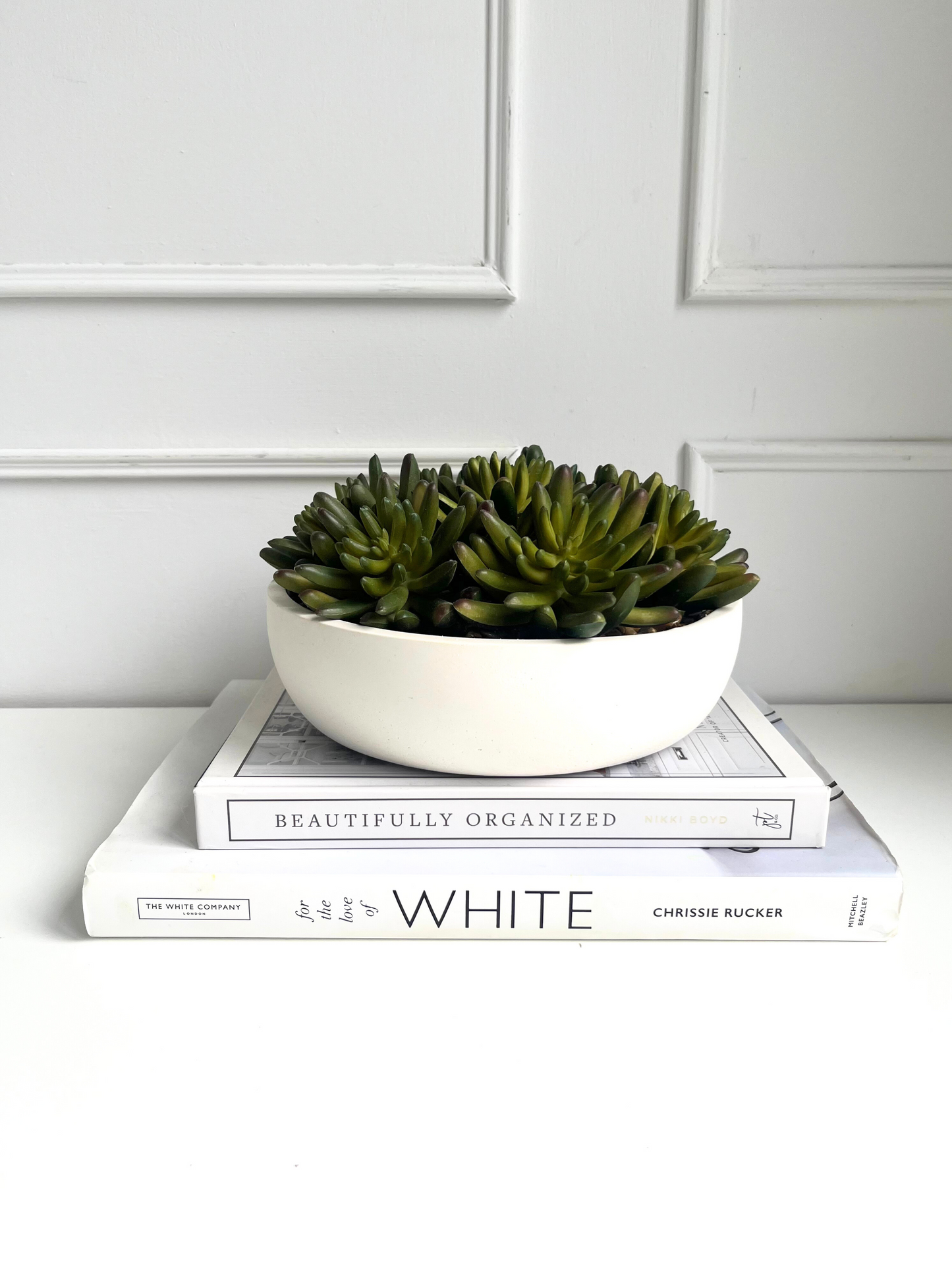 lush green artificial agave succulents set in stones in a cream colour eco resin bowl displayed on a stack of books.