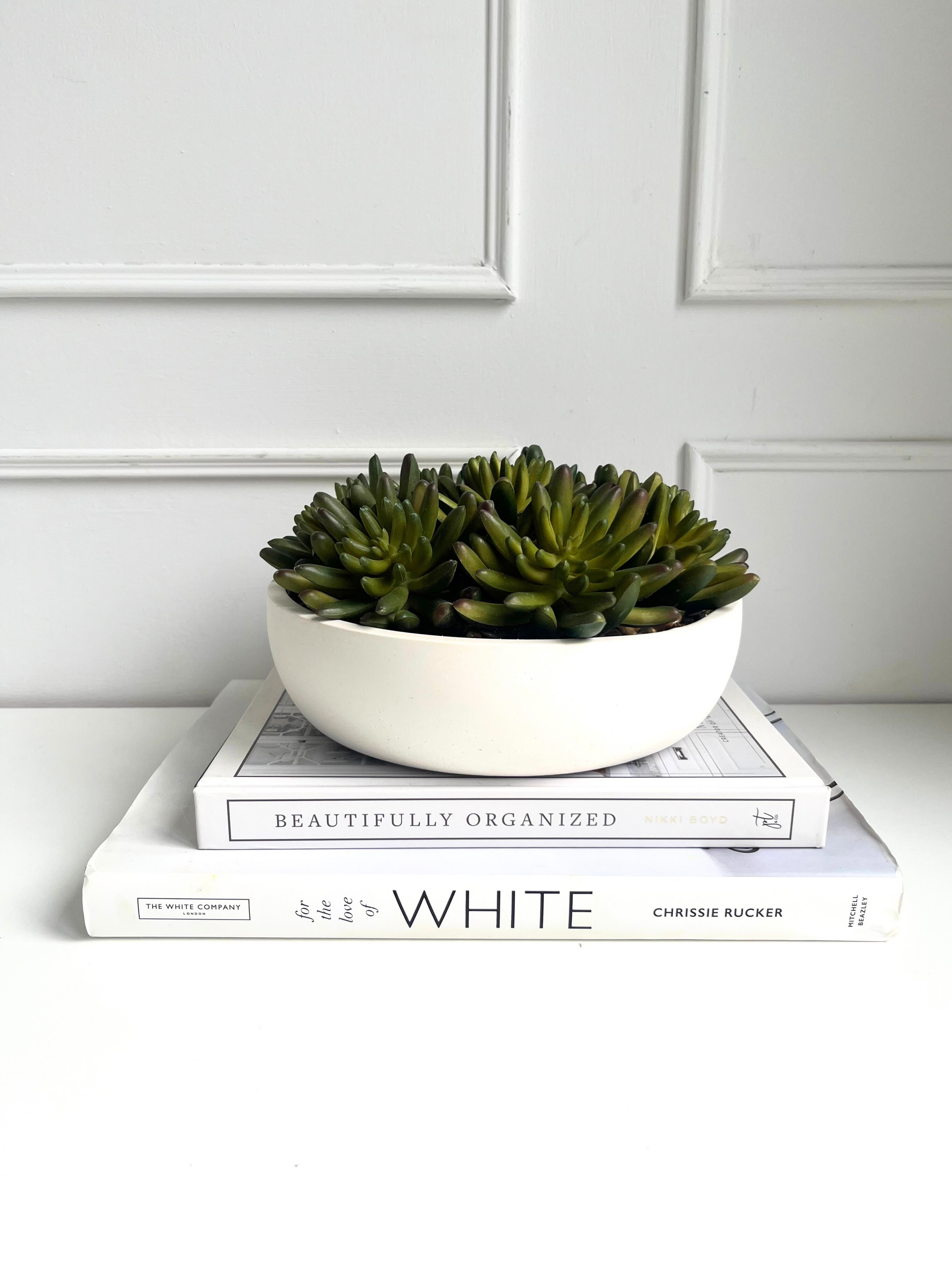 lush green artificial agave succulents set in stones in a cream colour eco resin bowl displayed on a stack of books.
