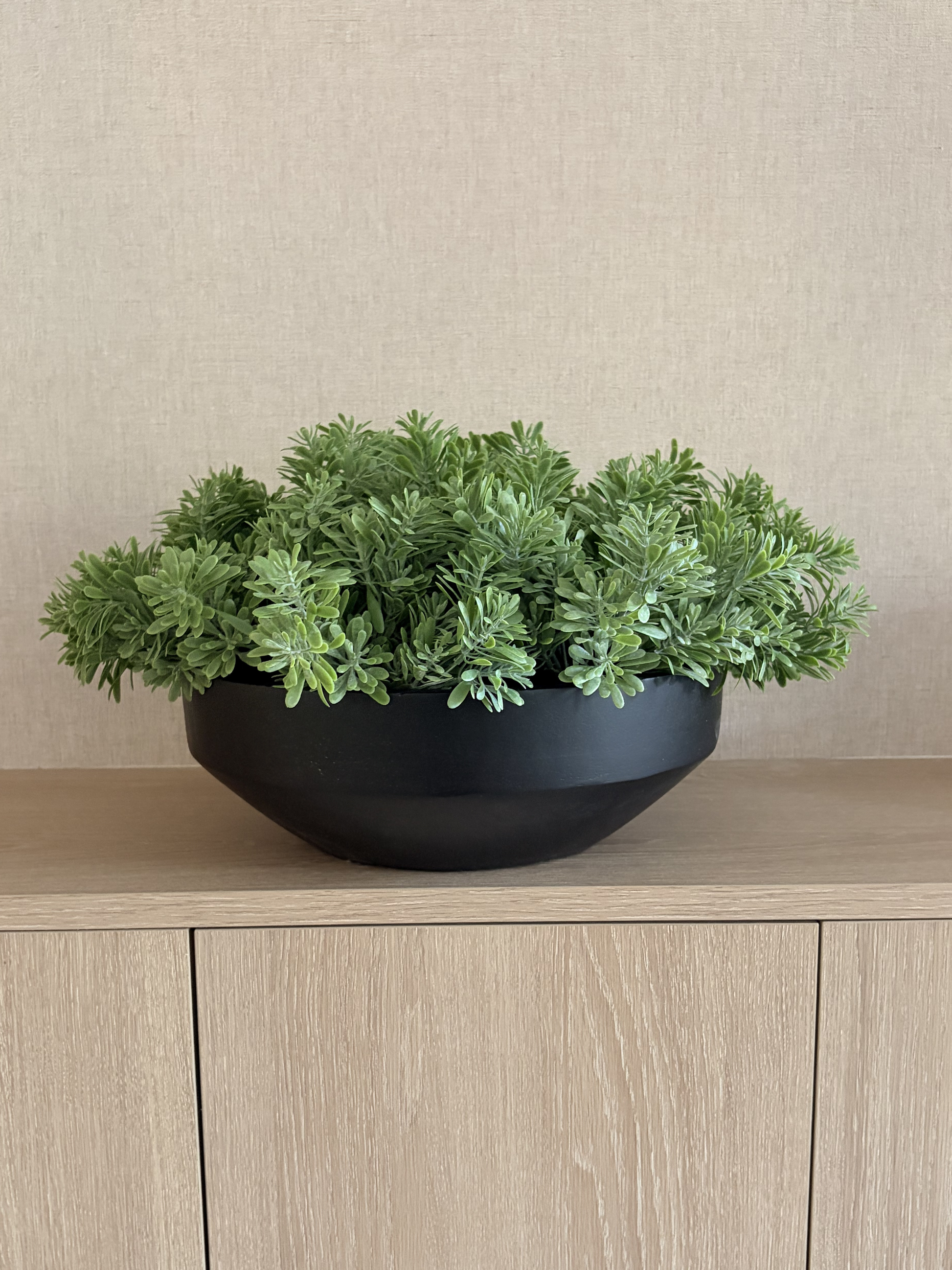 Lush green artificial crossestephium arranged in a black mango wood large bowl planter displayed on a wooden sideboard.