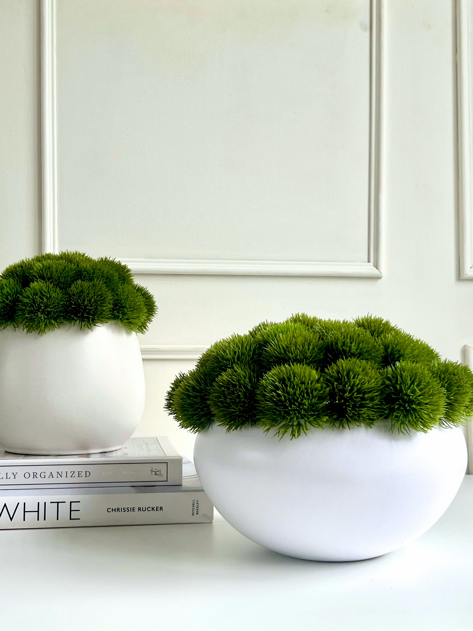 Vibrant green artificial dianthus set in a matt white plant pot displayed on a stack of books next to vibrant green artificial dianthus in matt white bowl planter.